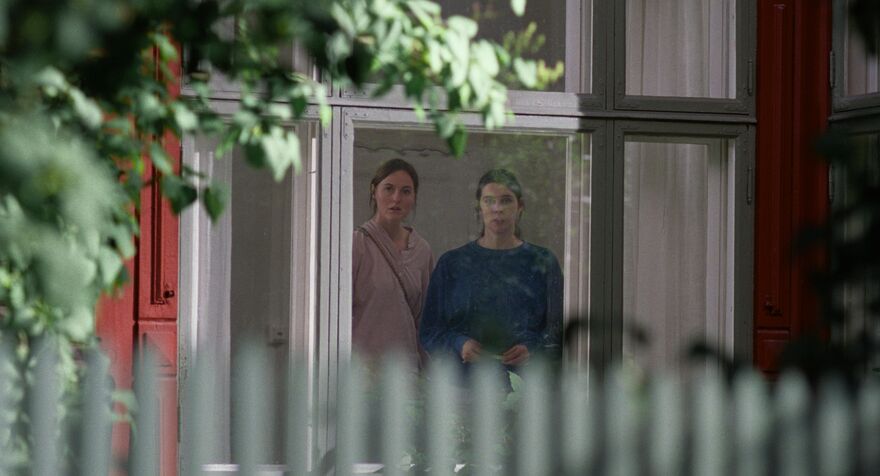 Two women look out of a window of a house
