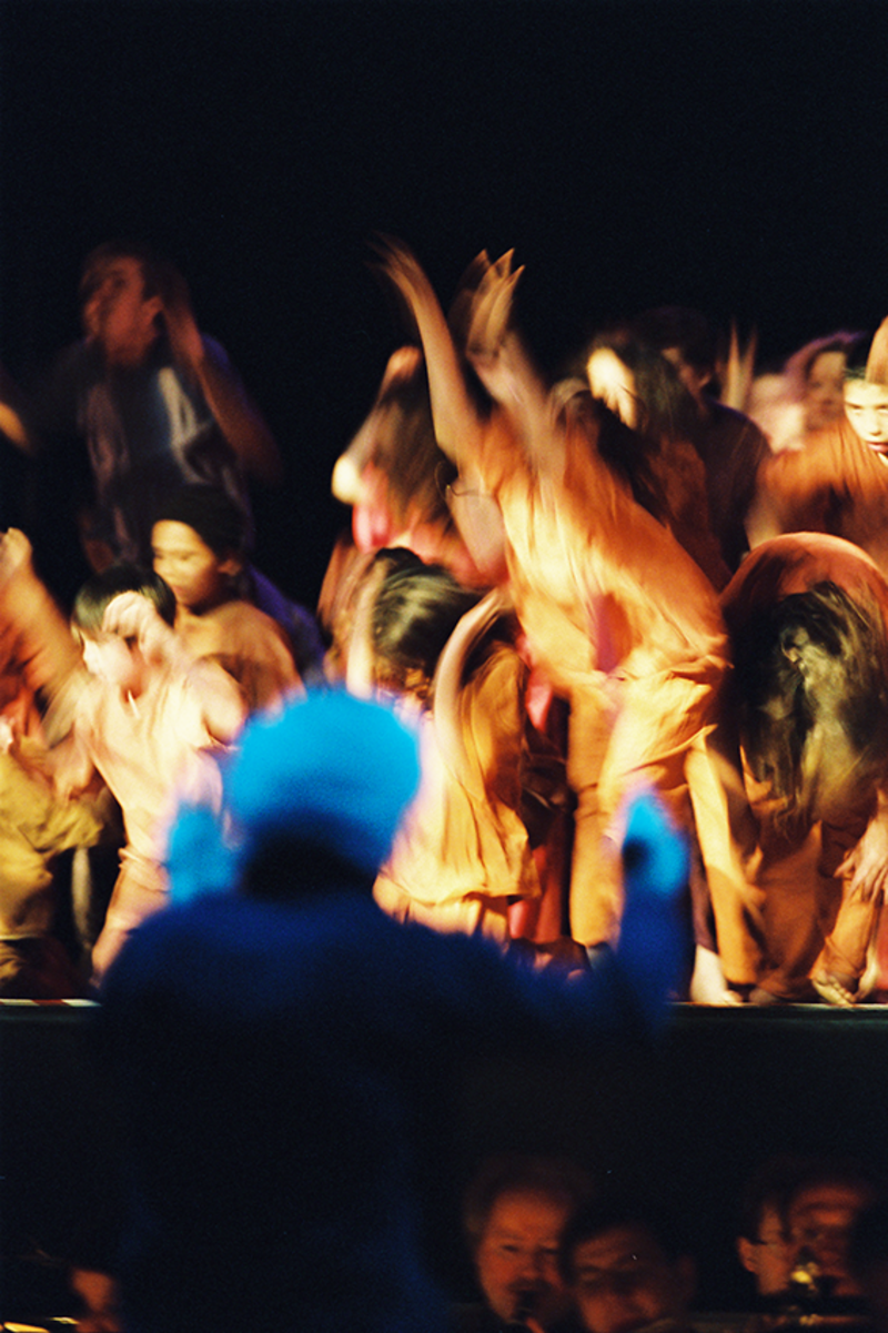 A blurry image of a conductor standing in front of a group of dancing people 