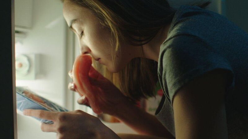 Woman standing at an open fridge smelling raw meat