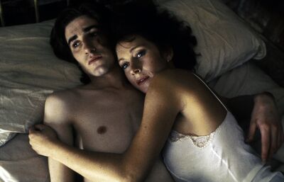 A worried man and woman hug in bed together.