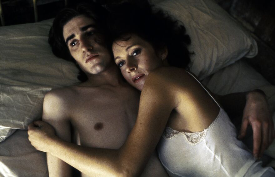 A worried man and woman hug in bed together.