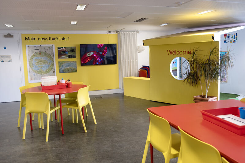 Create Space with red tables, yellow chairs and Make now, think later! display