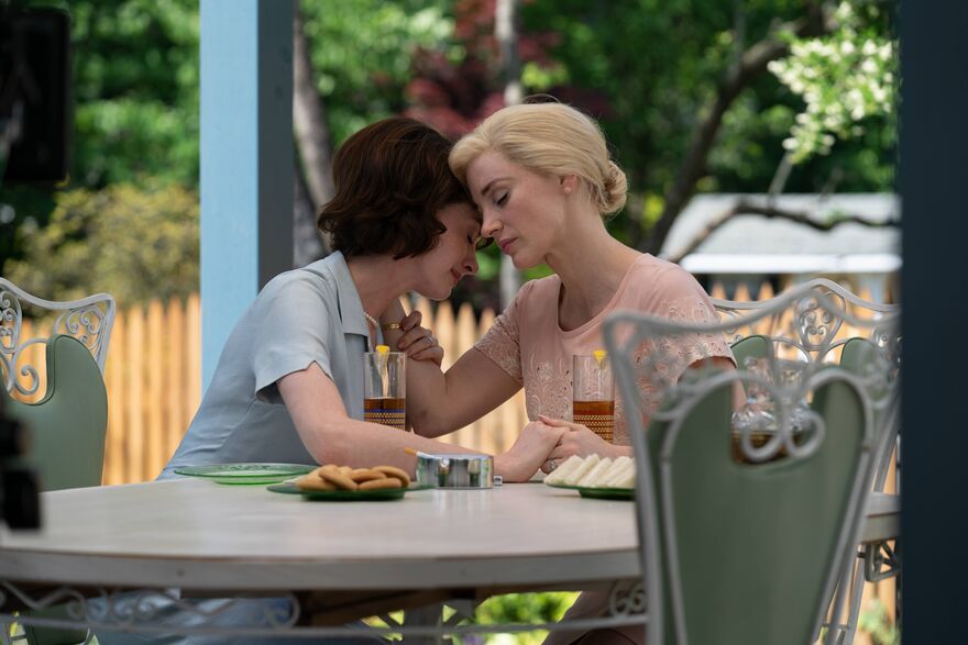 Two women embrace while sitting at an outdoor table.