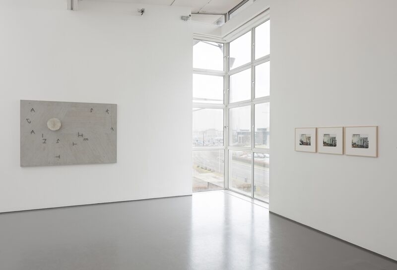 'Grey Gardens' exhibition in our galleries. A picture shows letters on the floor next to a circle. There are photographs of buildings on the other wall.