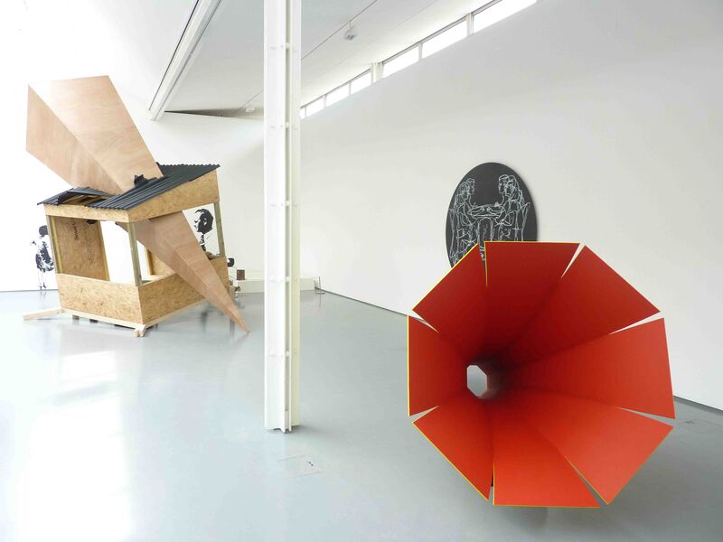 From exhibitions in Summer 2009. A large red object that looks like a gramophone lies in DCA galleries. Behind this, there is a wooden structure which is pierced by a large wooden pyramid.