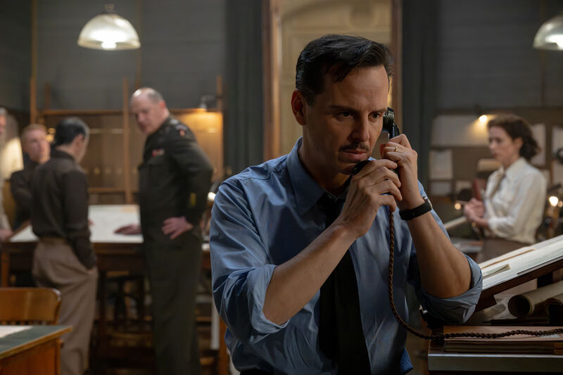 An anxious man takes a telephone call while watched by others in a war room