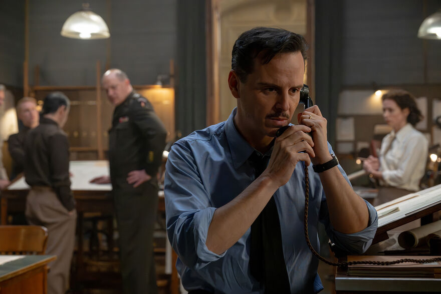 An anxious man takes a telephone call while watched by others in a war room