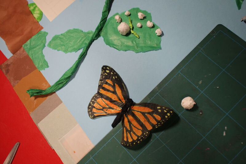 Paper butterfly on a table beside a leaf made from tissue paper