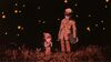 A little girl and a young boy stand in a field at night surrounded by fireflies