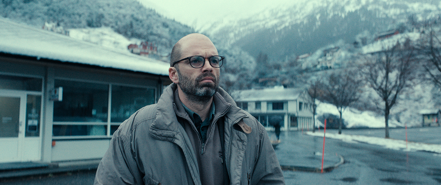 A man stands sadly outside of a municipal building in the Nordic scenery