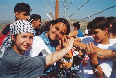 A group of Palestinian children smile for a photo next to a barbed-wire fence