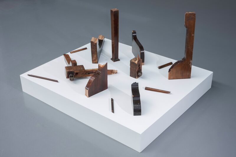 A structure from Continue Without Losing Consciousness, Broken up pieces of mahogany wood are displayed upright on a white plinth.