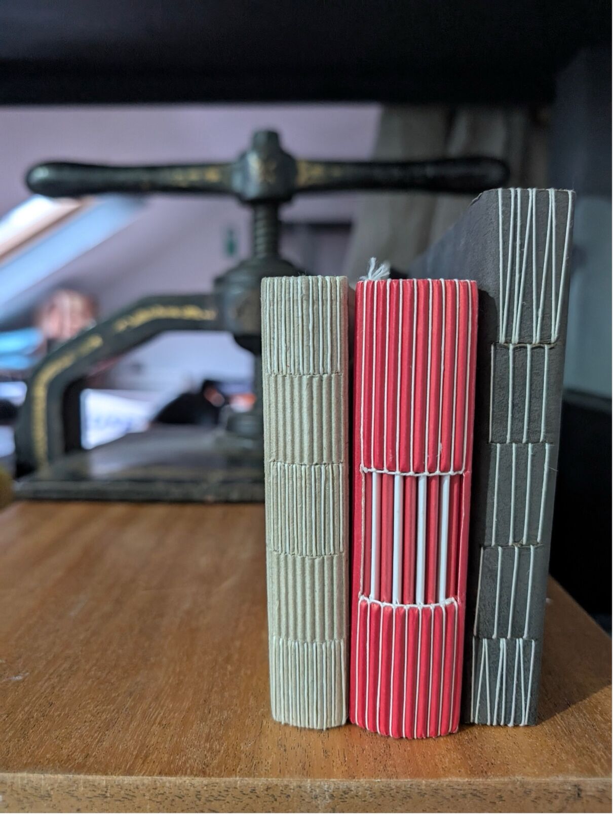 Three hand made books with different spine stitching infront of a press