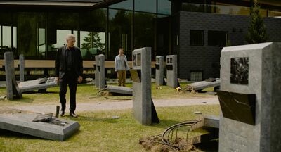 A man in a black suit stands in a futuristic graveyard.