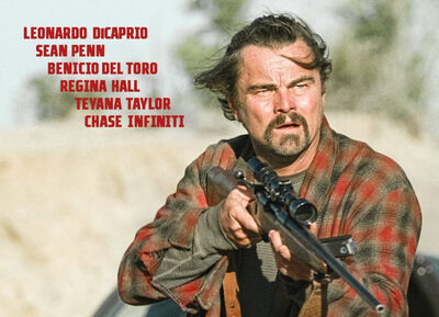 Leonardo DiCaprio wears a flannel t-shirt and points a rifle, his hair is blowing in the wind.