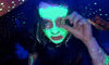 Teenage girl with face painted in florescent green holding a fake eye to her eye