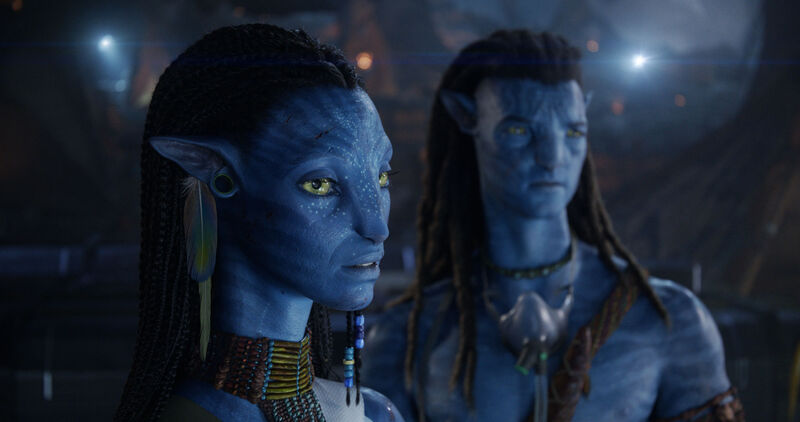 Two blue humanoid aliens wearing jewellery stand next to each other.
