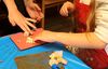 Child and adult pressing flowers onto a gelli plate covered in orange ink