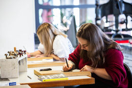 Two people sitting at a table in DCA Print Studio drawing designs onto lino