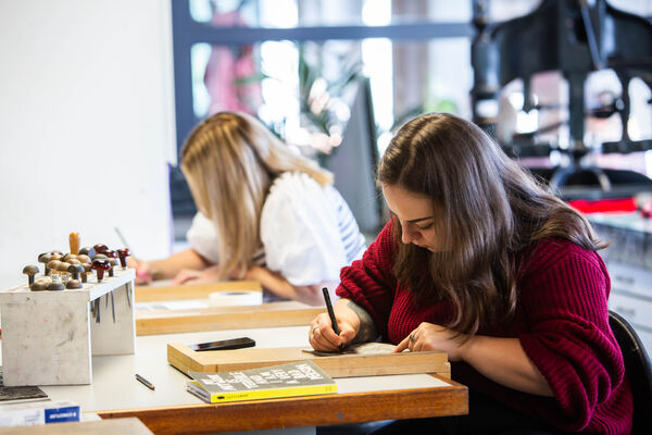 Two people sitting at a table in DCA Print Studio drawing designs onto lino