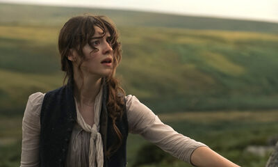 A dark haired woman stands in the rolling countryside.