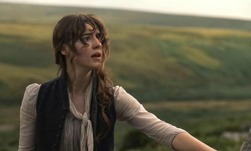 A dark haired woman stands in the rolling countryside.