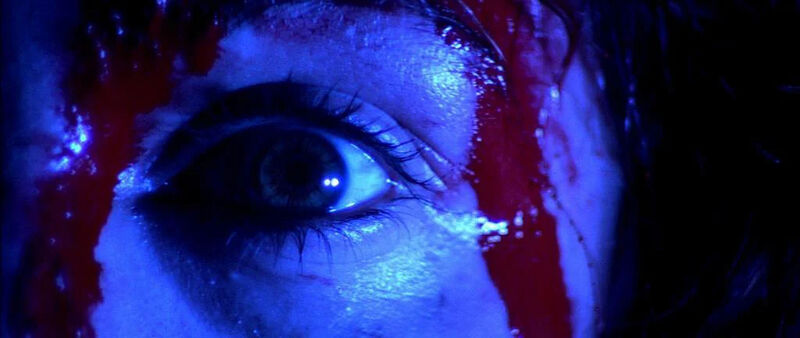 Close up of a persons eye. They are lit in blue with red blood running down their face