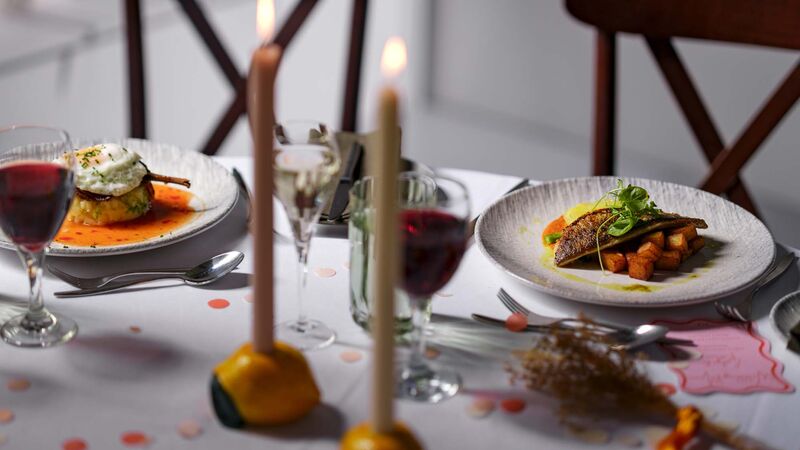 A table set with two meals and cutlery, glasses of wine and two candles