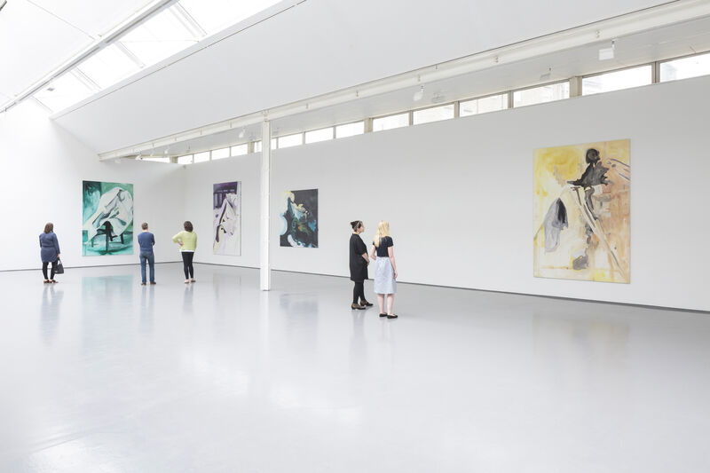 Installation view of a gallery with bright natural light and white walls. We can see four paintings from a distance. The paint strokes are bold and broad. A few people look at the paintings, dispersed through the gallery.