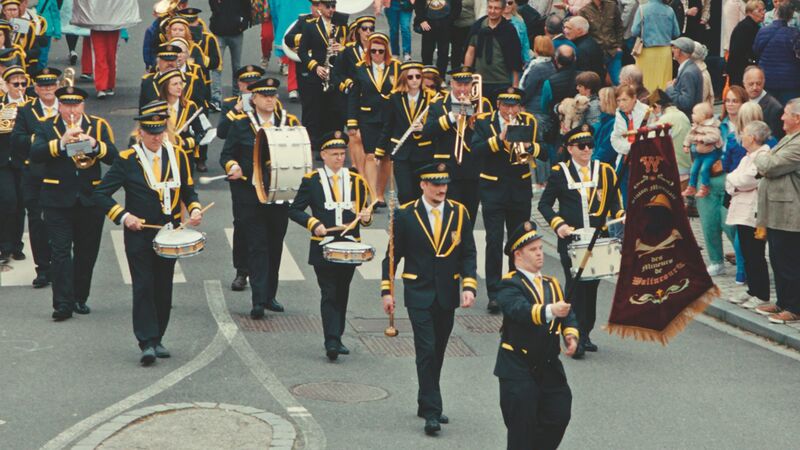 A marching band in black and yellow uniforms take part in a procession