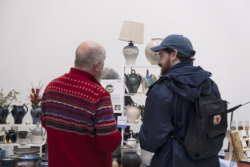 Two men talking in front of a craft stall showcasing ceramics