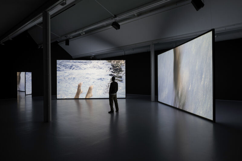 Installation documentation of gallery two, showing a two channel film projected across two big screens positioned at an angle to each other. The gallery is dark. 