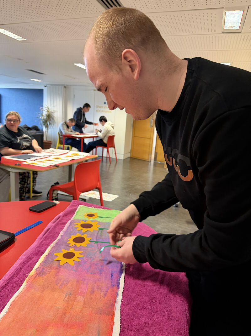 Person laying out vinyl shaped like sun flowers onto painted fabric