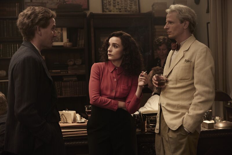 A woman and two men stand and talk over drinks