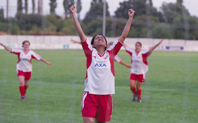 A teen girl footballer raises her hands in triumph