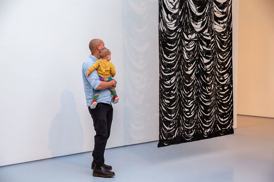 A man and baby look at a hanging artwork at DCA Galleries