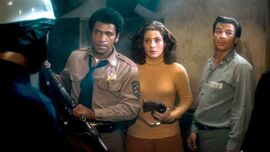Police officer, woman and prisoner stand in front of a man in a helmet