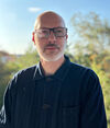 A white man wearing dark framed glasses looks into the distance