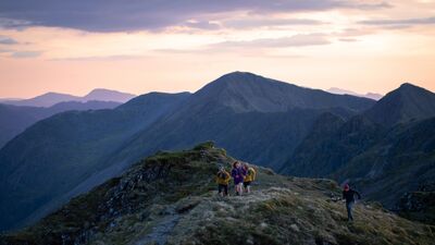 Three people jog up a mountain range as the sun rises