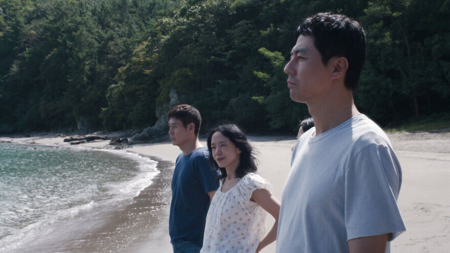 Two men and a woman stand on a beach looking out at the water