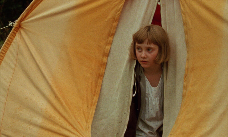 A girl peers out from a yellow tent