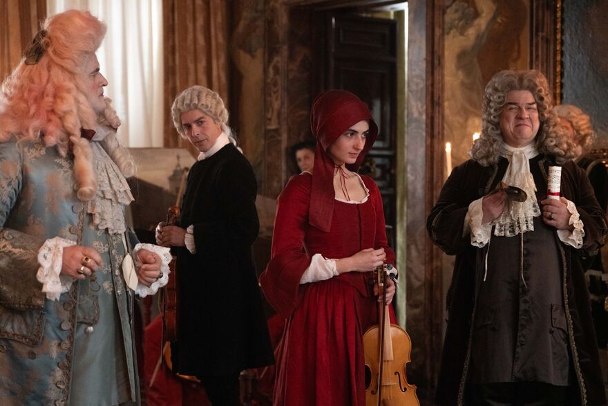A lady in red period costume is holding a violin with noblemen on either side looking gleeful, a man in the background looks on in secret