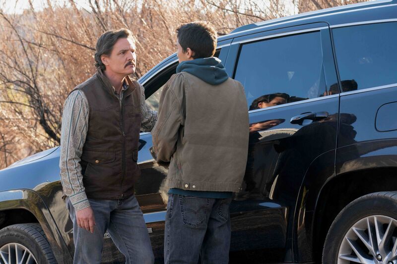 A man wearing a fillet looks at a teenage boy outside of a car.