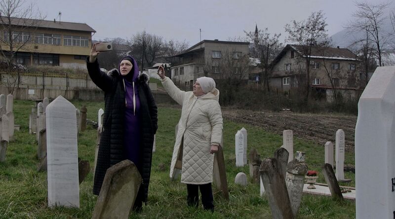 Two women stand in a graveyard holding up a phone camera.