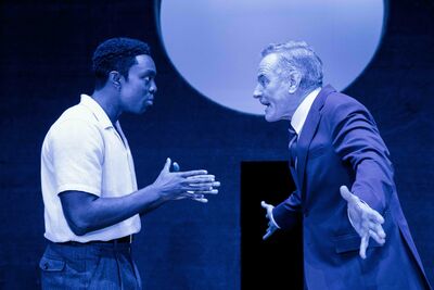 Against blue lighting, two men have an argument on stage
