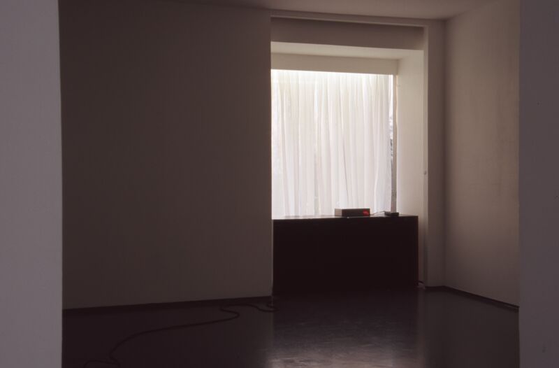 A small box with a red light on it sits on a black table in an empty room.