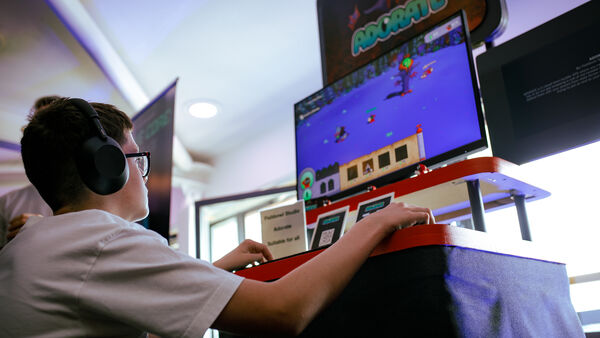 A child wearing headphones looks up at a monitor while playing a video game at Drop in and Play