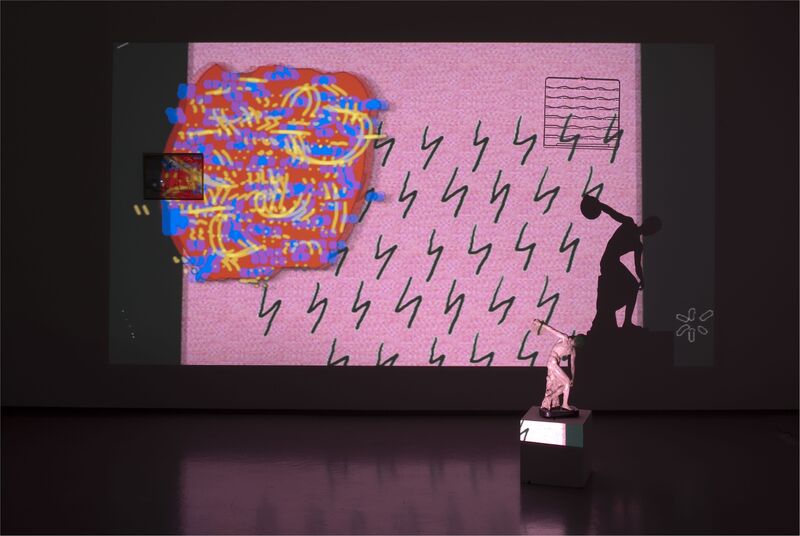DCA Galleries during Trisha Baga's exhibition. A projections screen shows a pink background with red, yellow and blue swirls on top. A  small statue of a woman sits in front of the projection.