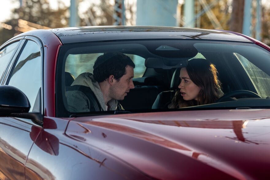A man and a woman are sat in the front seats of a red car having a serious discussion