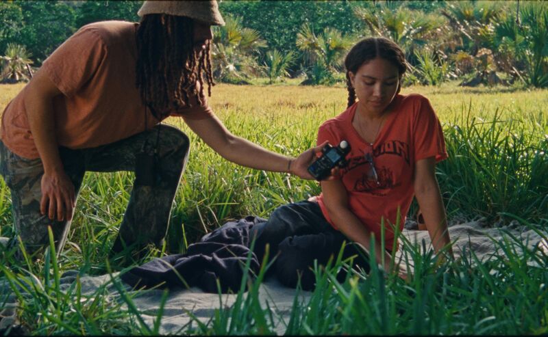 A person holds a microphone in front of a woman's face while she sits on the grass.